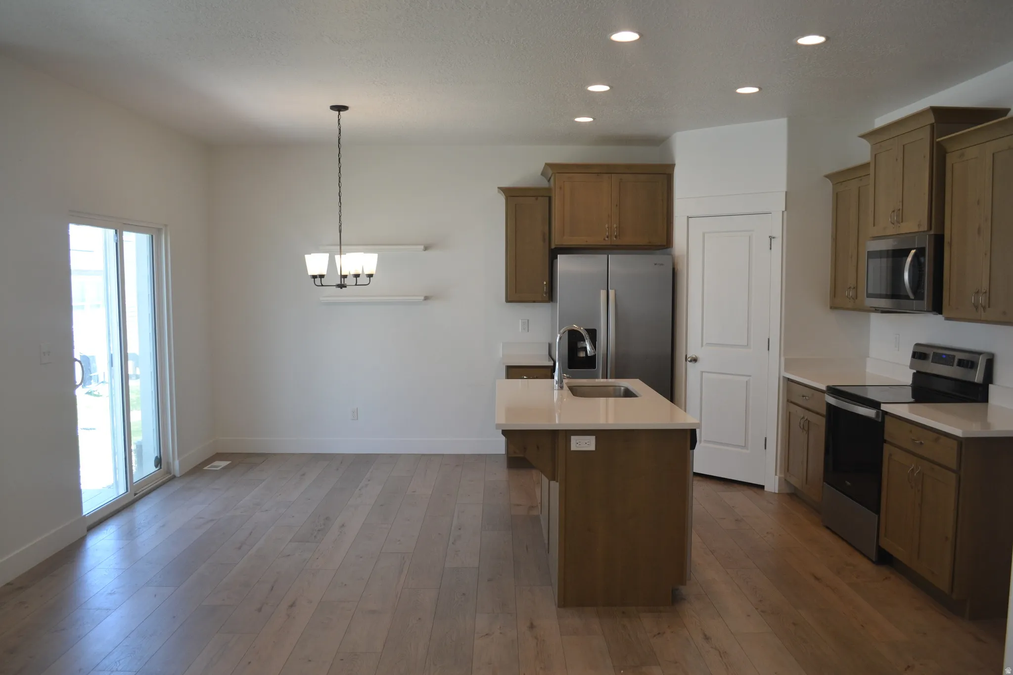 Open-concept kitchen and dining area featuring wood-finish flooring, recessed lighting, and a sliding glass door