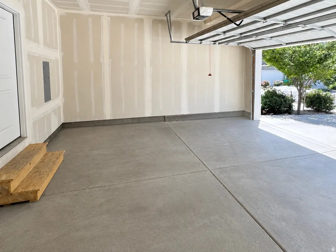 Spacious garage featuring a concrete floor, an overhead garage door with an automatic opener, a side entry door, and exposed drywall