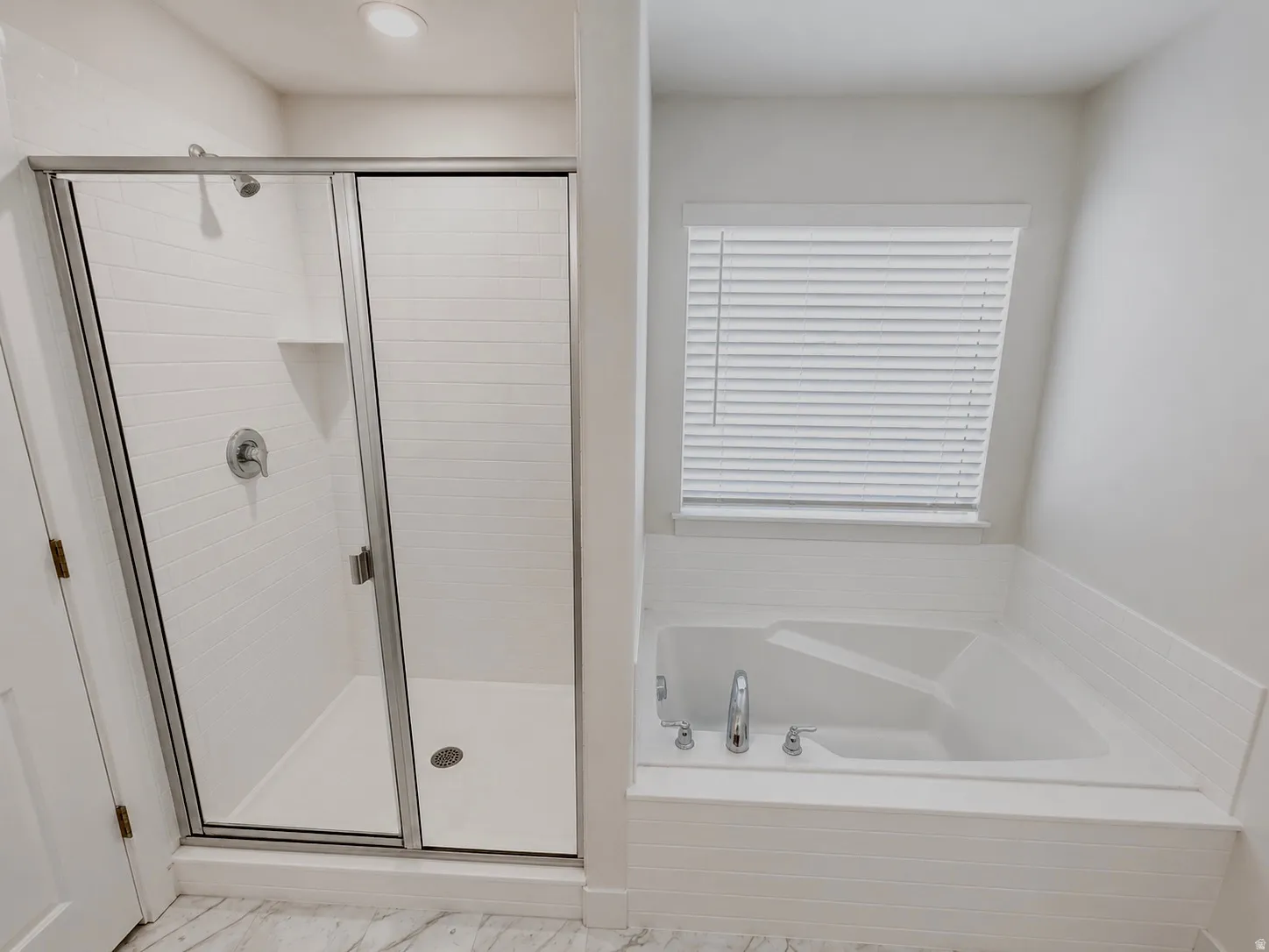 Corner soaking tub with tile surround, adjacent to a glass-enclosed shower featuring white subway tile, a built-in shower shelf, and a ceiling-mounted light fixture