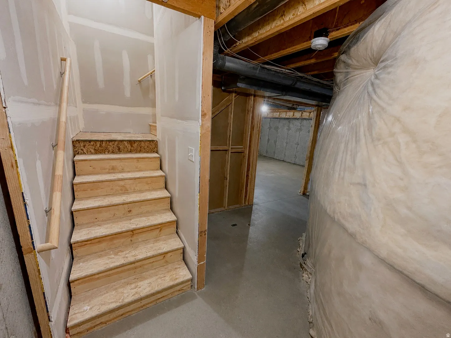 Unfinished basement featuring exposed wood joists, concrete flooring, and framed walls