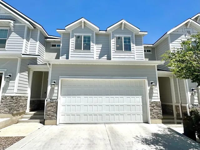 Light gray siding exterior with stone accents, featuring a two-car garage, concrete driveway, and dormer windows