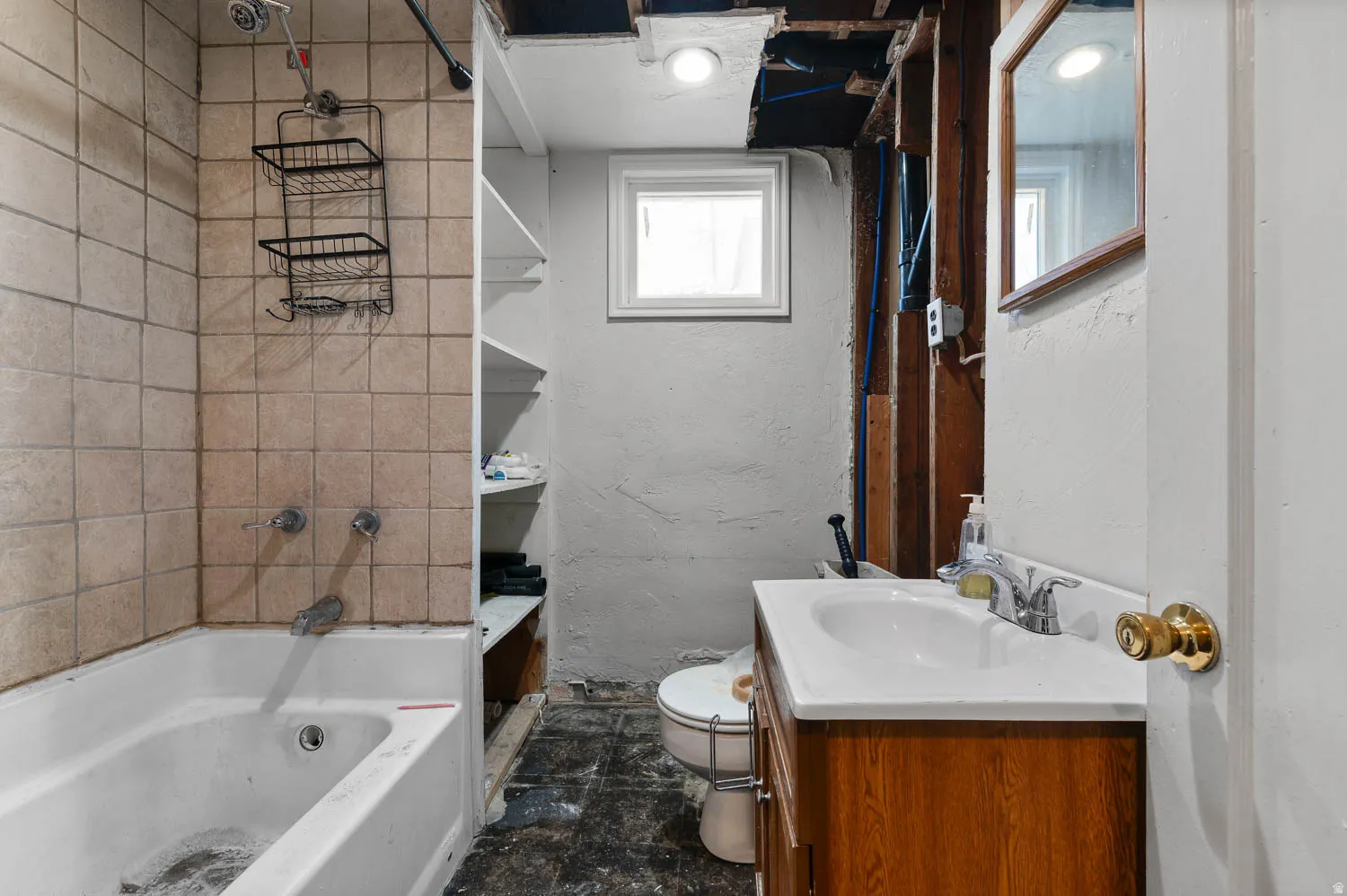 Bathroom featuring a white bathtub, tiled shower surround, integrated shelving, and a vanity with a white sink and wood-finish cabinetry