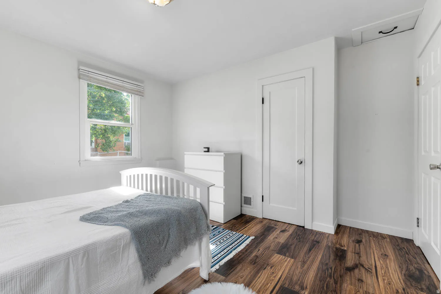 Bright room featuring rich wood-finish flooring, white walls, and a window with blinds