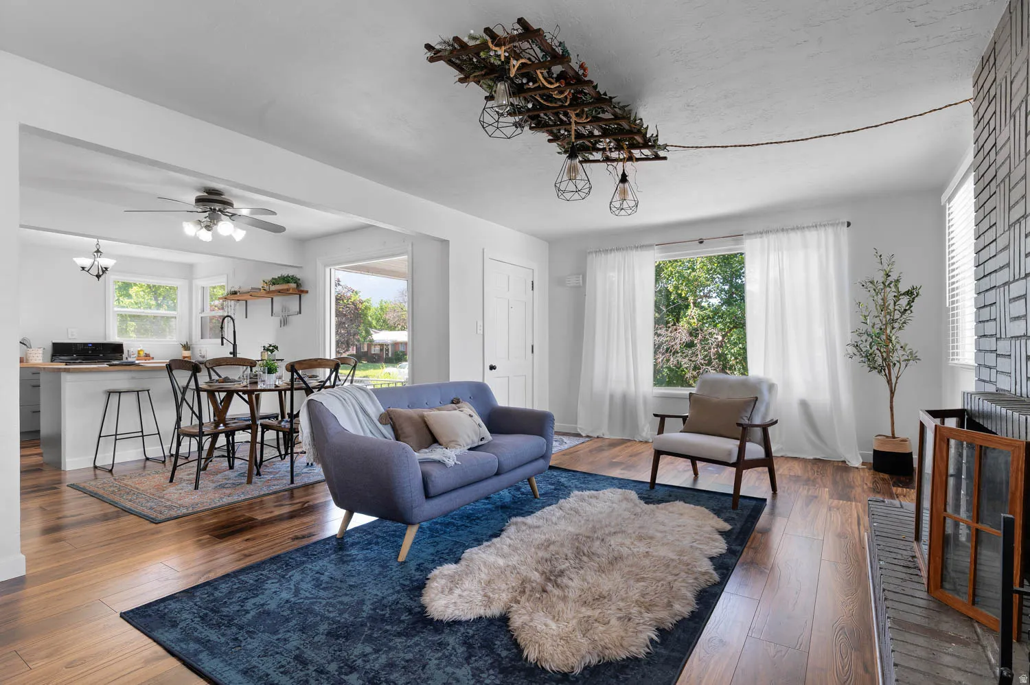 Open-concept living area featuring rich wood-finish flooring, a contemporary ceiling light fixture, and a patterned brick fireplace surround