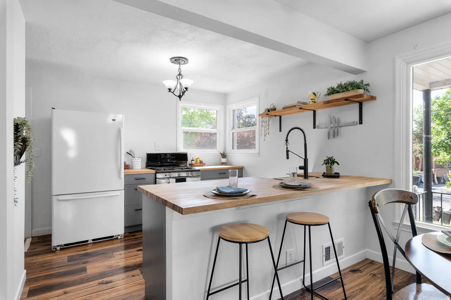 Kitchen featuring wood-finish flooring, two windows, a white refrigerator, a black range with a microwave above, and light gray cabinetry