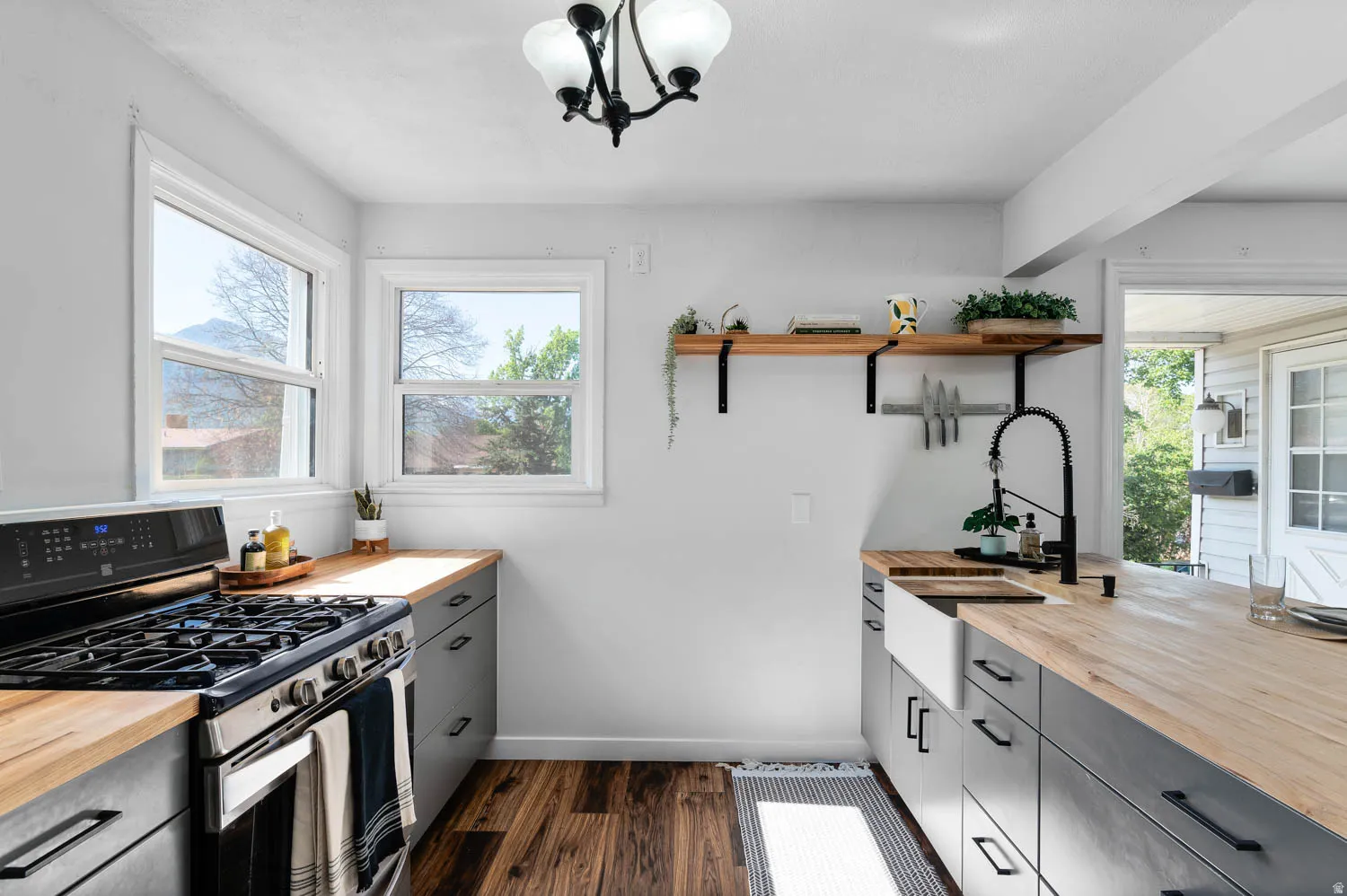 Modern kitchen featuring wood-finish countertops, dark cabinetry with matte black hardware, and stainless steel appliances