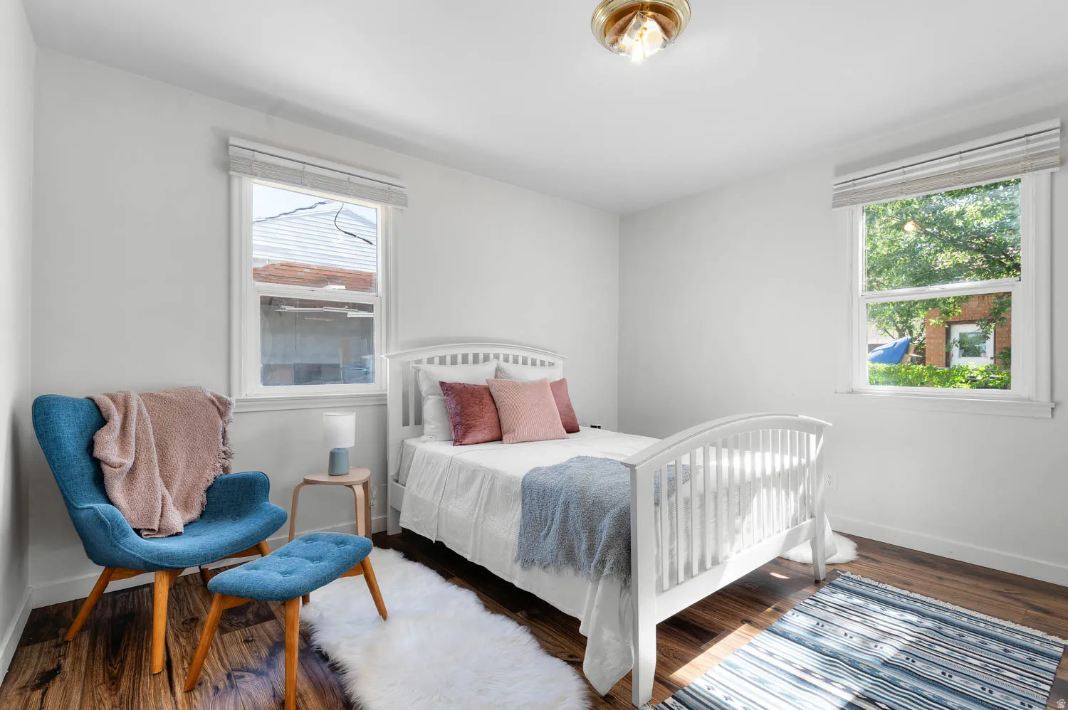 Bright room featuring wood-finish flooring, white walls, two windows with blinds, and a brass-tone flush-mount light fixture