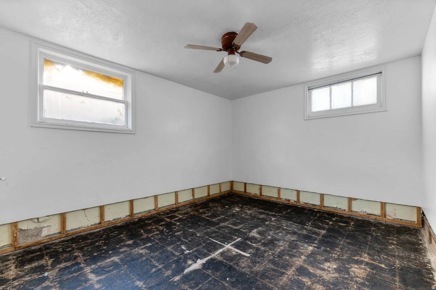 Room featuring a ceiling fan with light fixture, two windows, and exposed wall framing along the perimeter