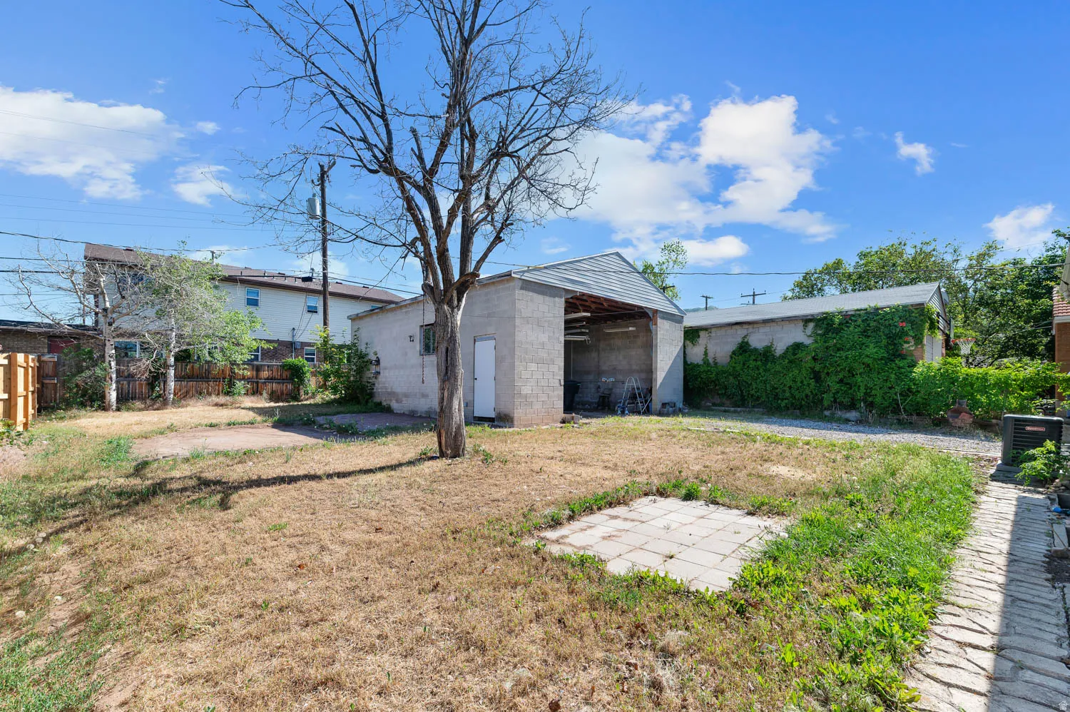 Expansive backyard featuring a detached garage with an open bay, a separate storage structure, a mature tree, and a paved walkway