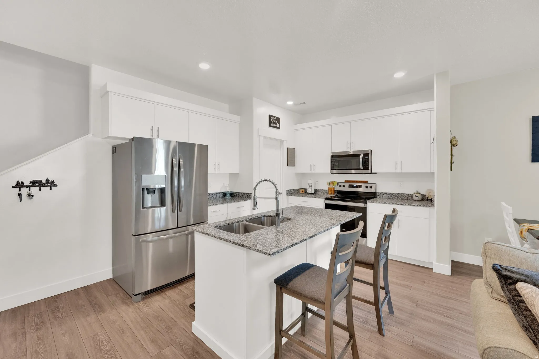Kitchen with white cabinetry, stainless steel appliances, granite countertops, and a central island with a double basin sink