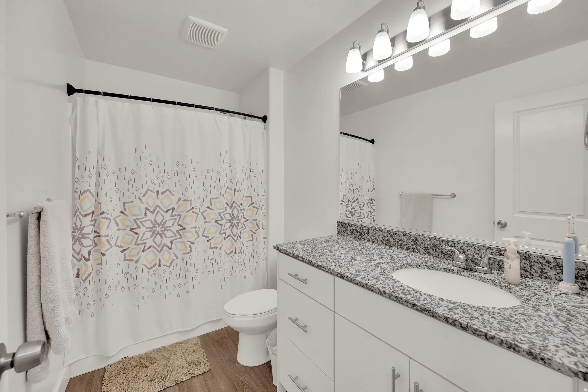 Bathroom featuring a white vanity with a speckled countertop, undermount sink, and chrome fixtures