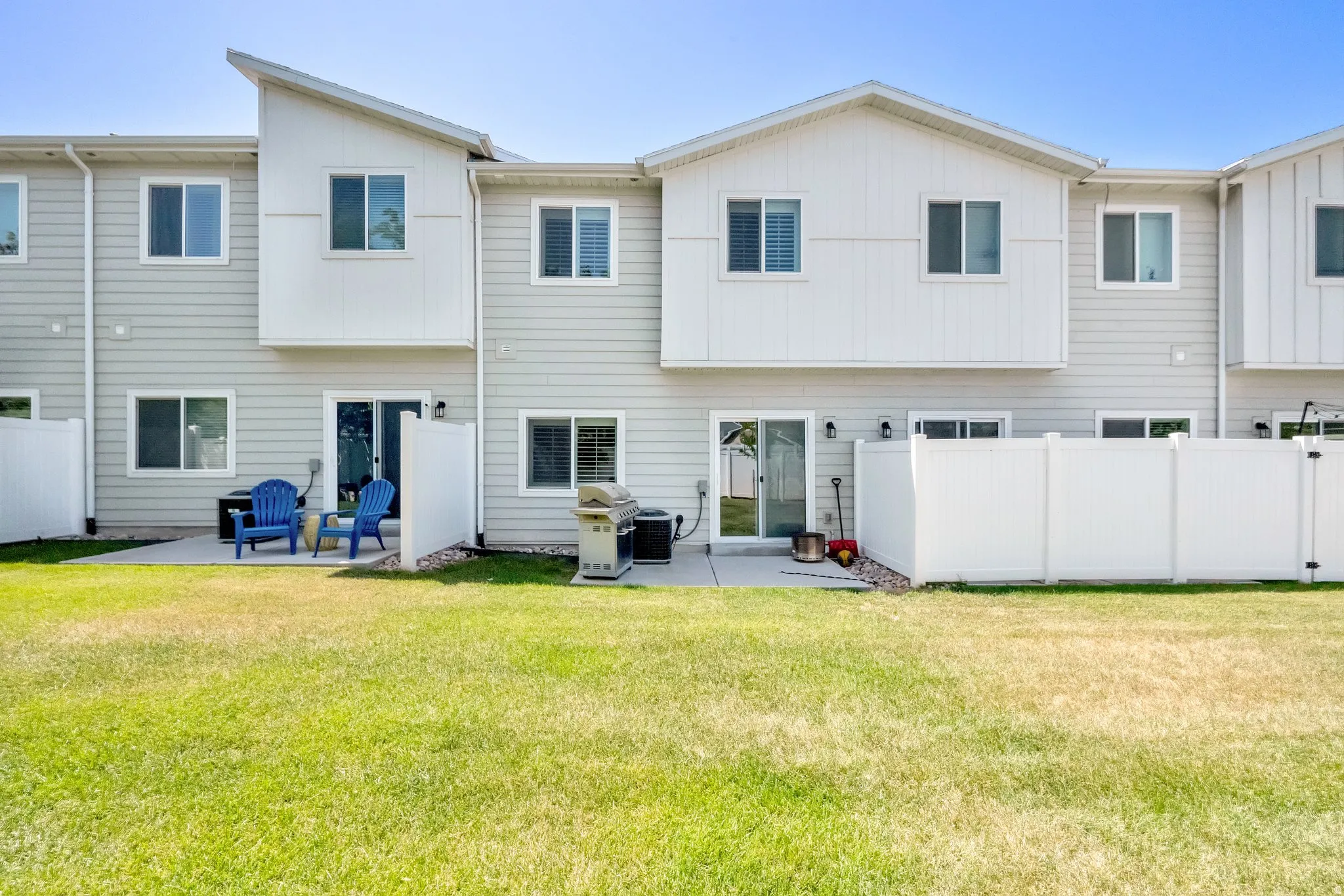 Rear exterior featuring light-colored siding, a private patio, sliding glass doors, white vinyl fencing, and a manicured lawn