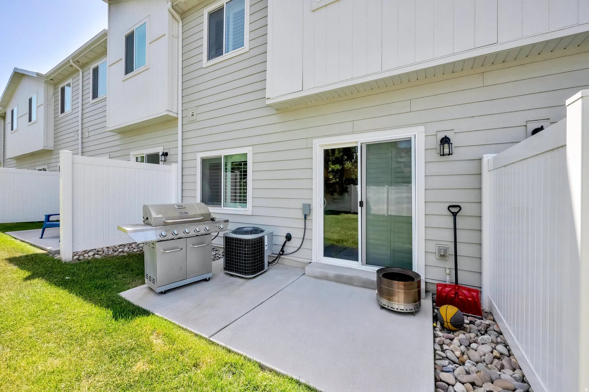 Private patio area featuring a sliding glass door entry, exterior wall lantern, and a stone-filled border