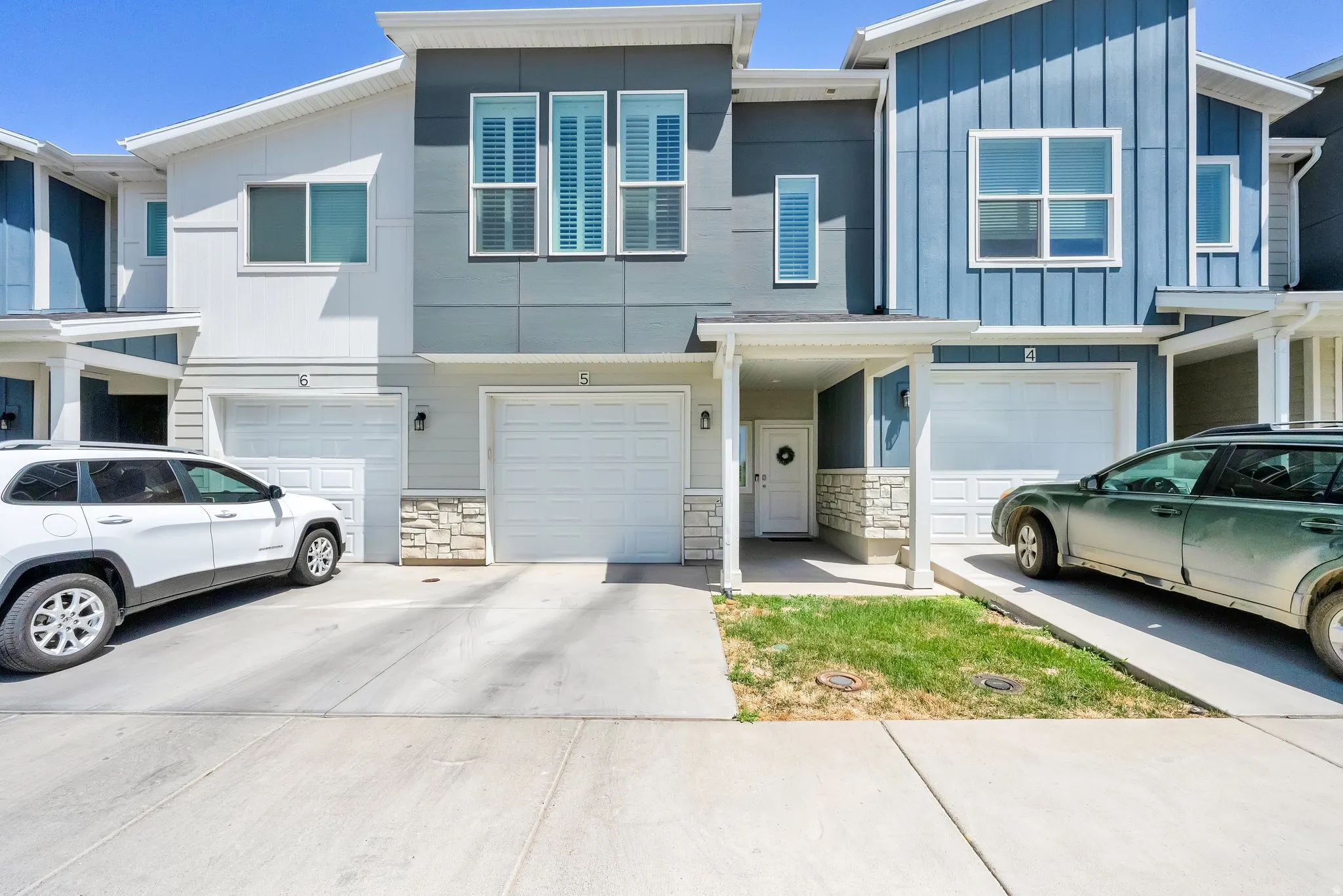 Modern townhome exterior featuring a white entry door with a wreath, a covered porch, stone veneer accents, and an attached garage with a white door