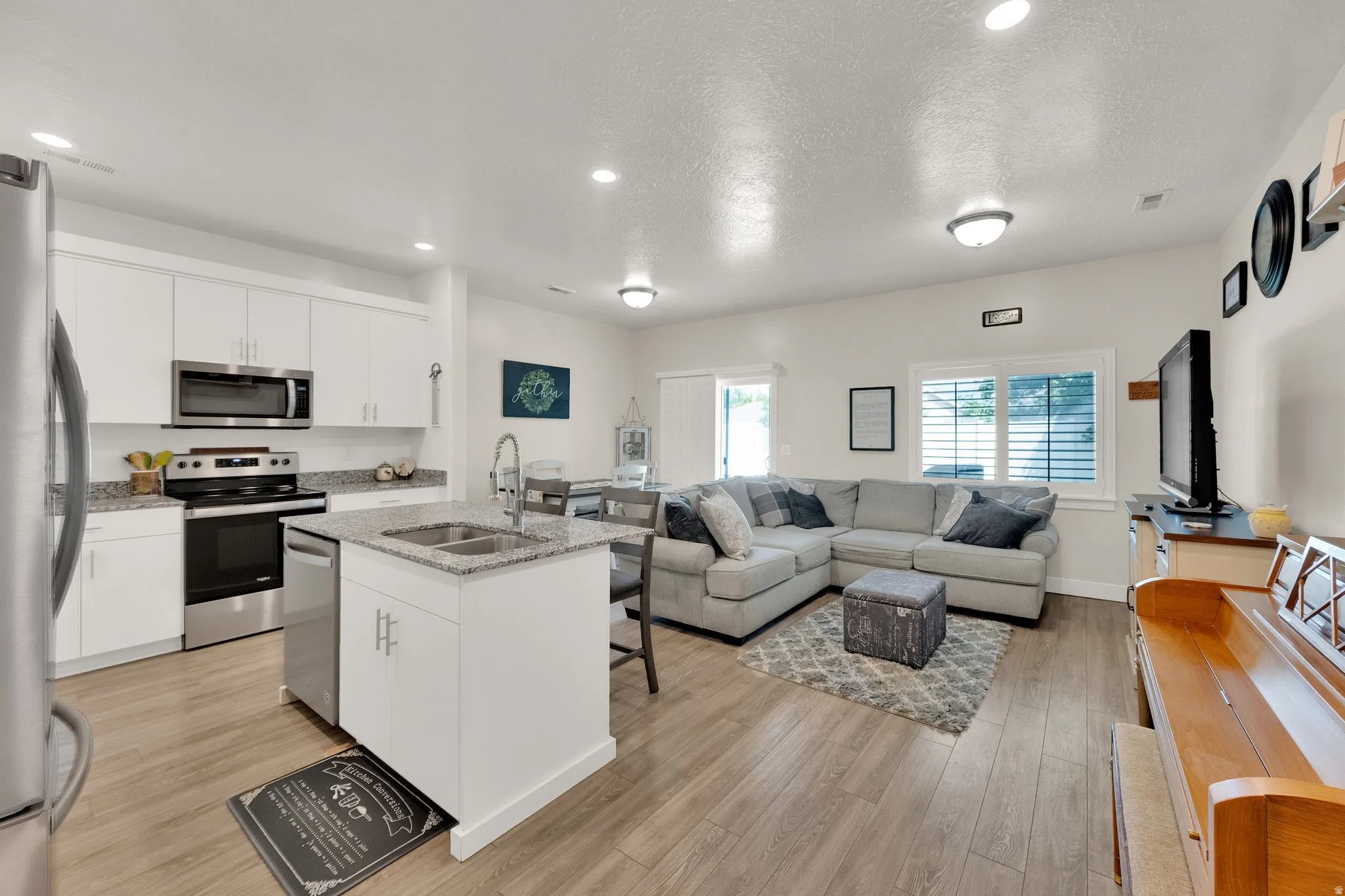Open-concept living space featuring wood-finish flooring, recessed lighting, and a kitchen island with an undermount double sink