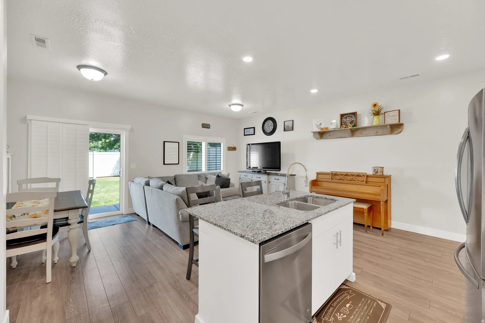 Open-concept living space featuring wood-finish flooring, recessed lighting, and a kitchen island with a double basin sink and stainless steel dishwasher