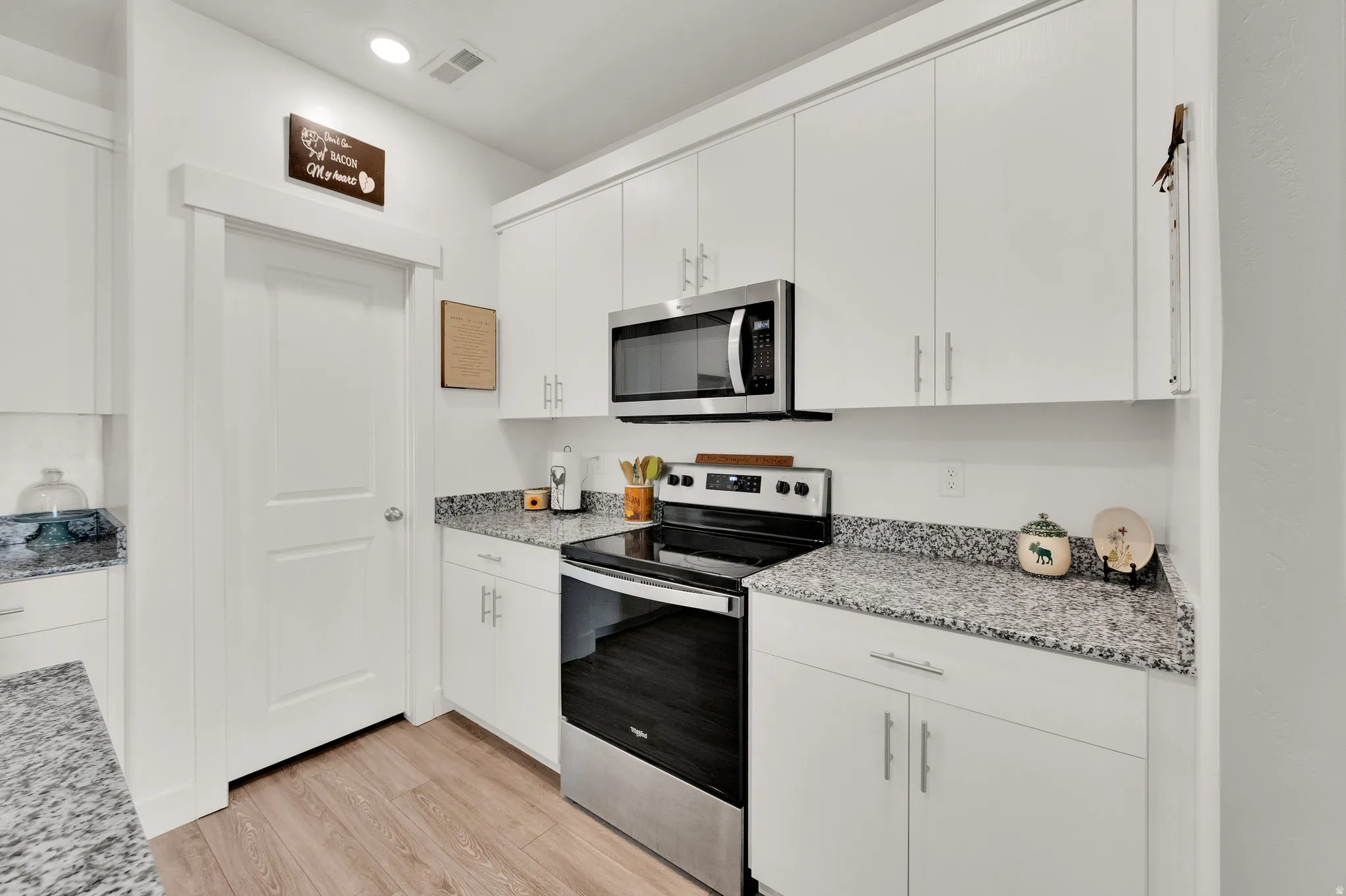 Modern kitchen featuring white cabinetry, stainless steel appliances, speckled countertops, and wood-finish flooring