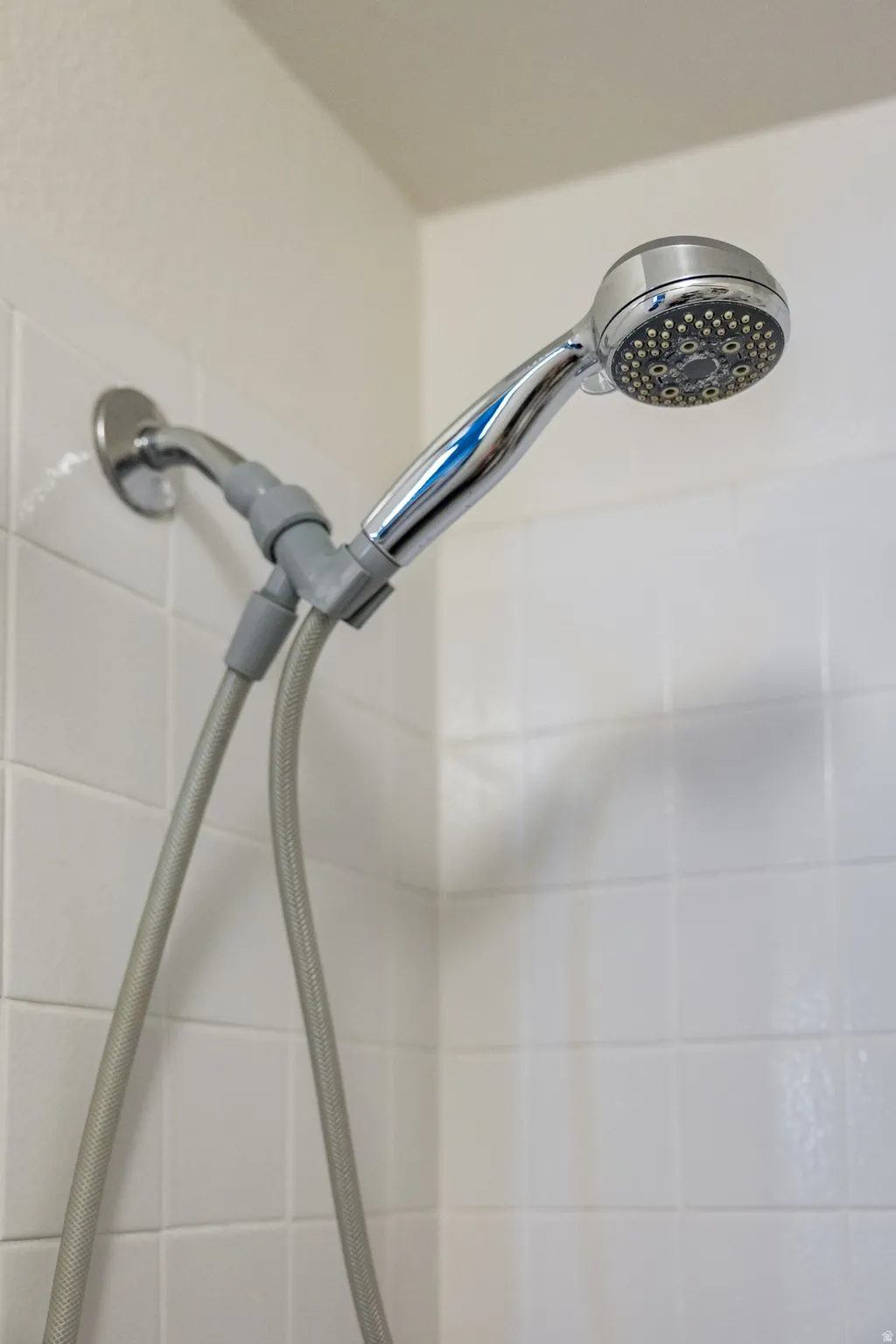 Shower fixture featuring a chrome finish, white subway tile surround, and a flexible hose