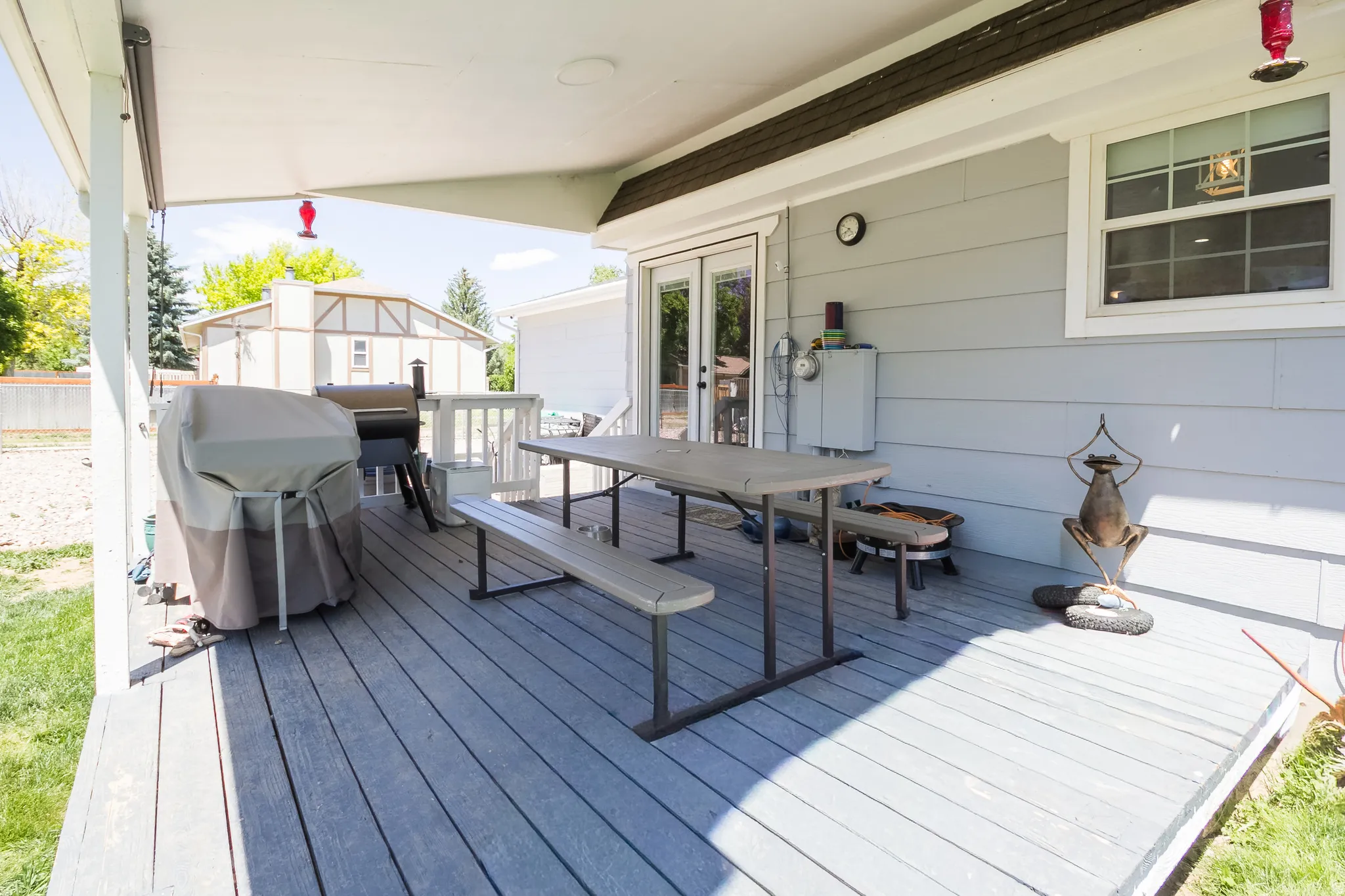 Spacious covered deck featuring composite decking, light gray siding, and double glass doors