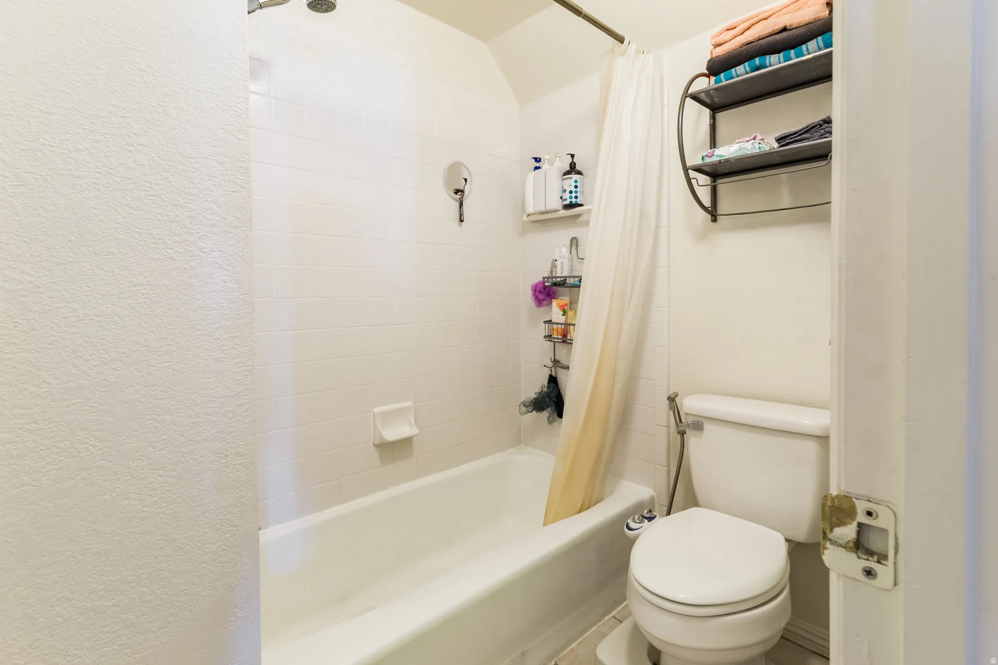 Bathroom featuring a white bathtub, white tiled shower surround, shower curtain rod, and a toilet