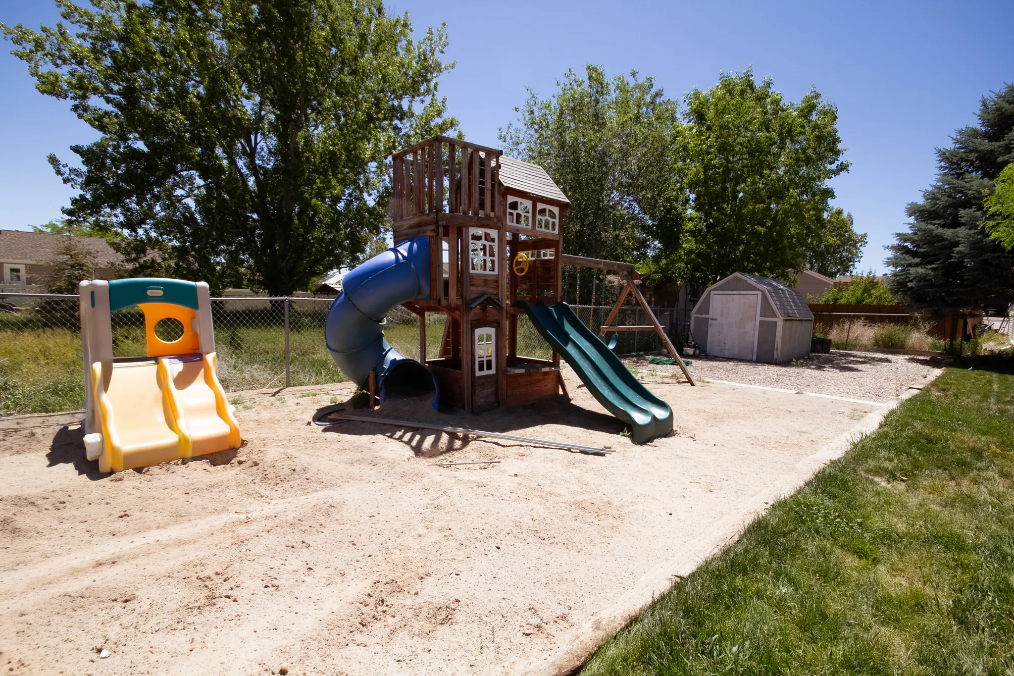 Backyard recreation area featuring a multi-level wooden play structure with slides and swings