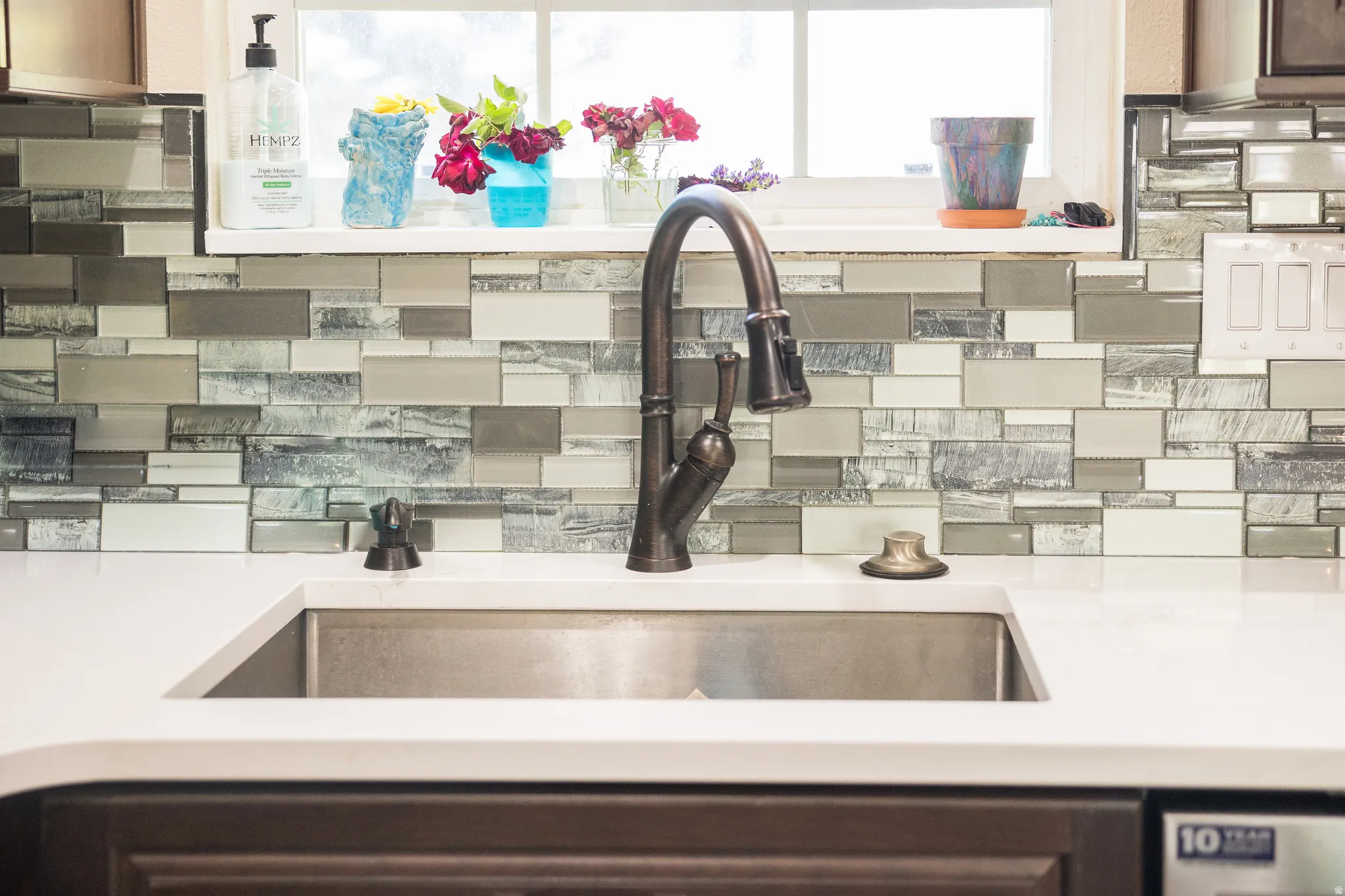 Kitchen sink featuring a brushed bronze gooseneck faucet, an undermount stainless steel sink, and white countertops