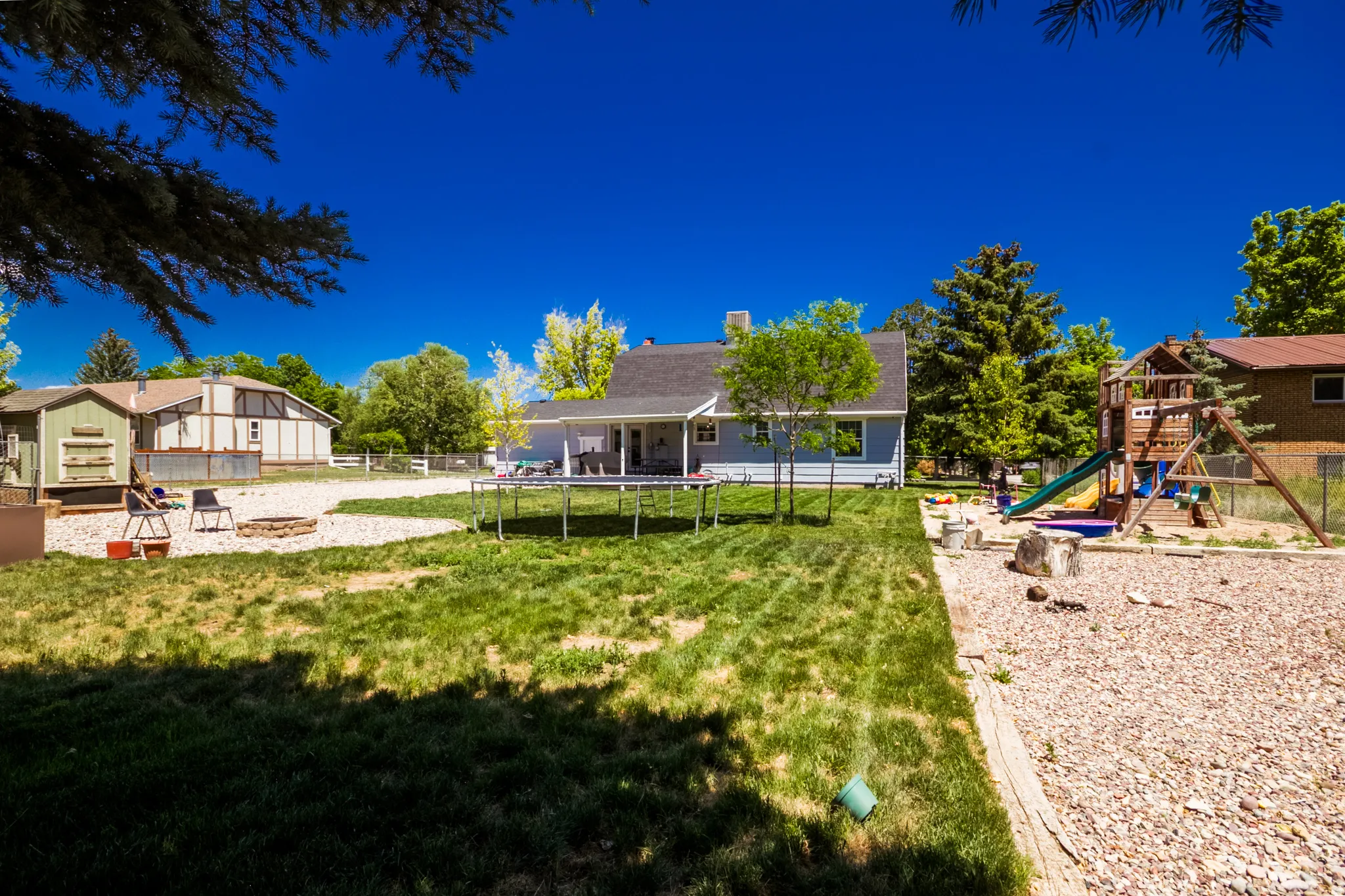 Expansive backyard featuring a large lawn area, a dedicated gravel fire pit area, and a separate gravel play area