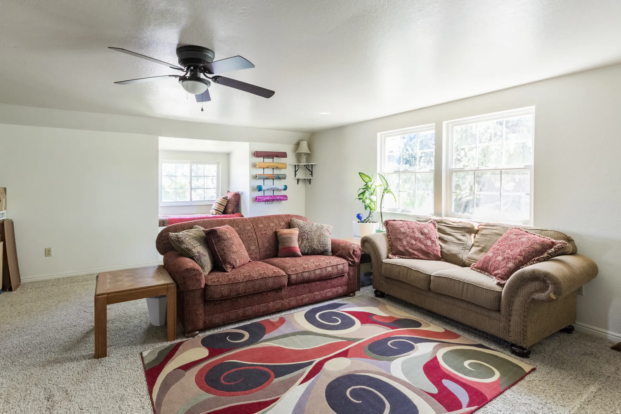 Living area featuring carpet flooring, a ceiling fan with integrated lighting, and multiple windows providing natural illumination
