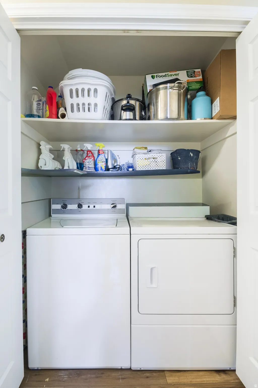 Dedicated laundry closet featuring a white washing machine and dryer, wood-finish flooring, white bifold doors, and two integrated storage shelves