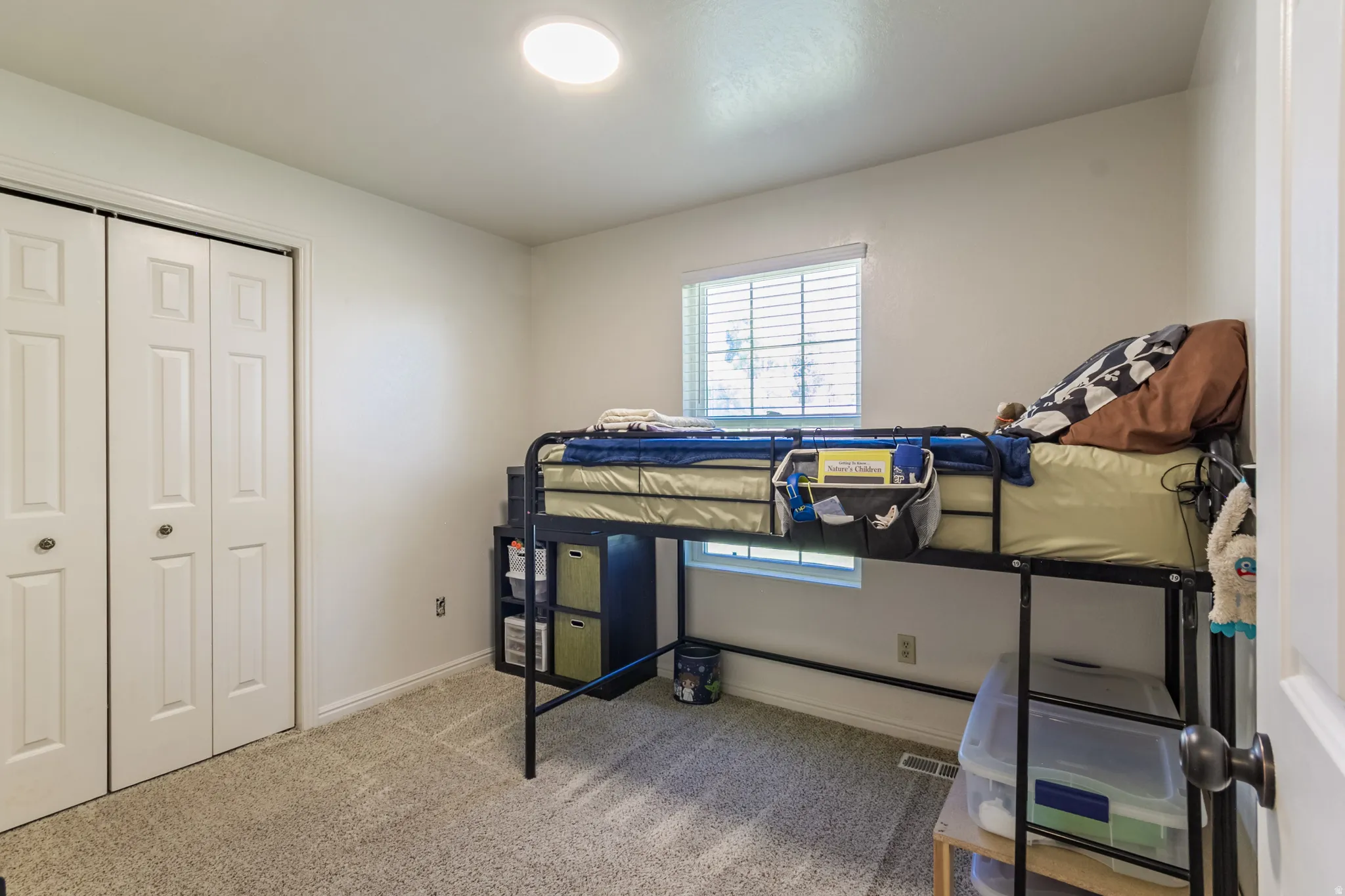 Interior room featuring neutral wall paint, carpet flooring, a window with horizontal blinds, and a bi-fold closet door