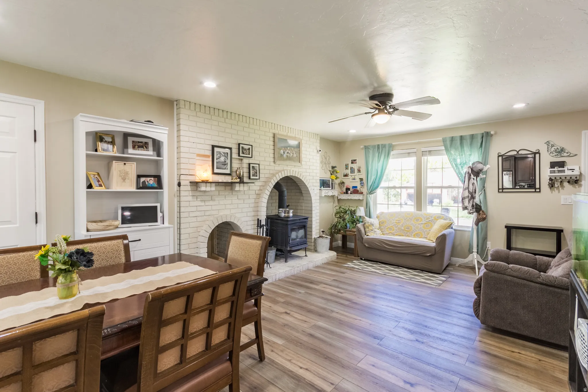 Open-concept living area featuring wood-finish flooring, recessed lighting, and a white brick fireplace with an arched opening