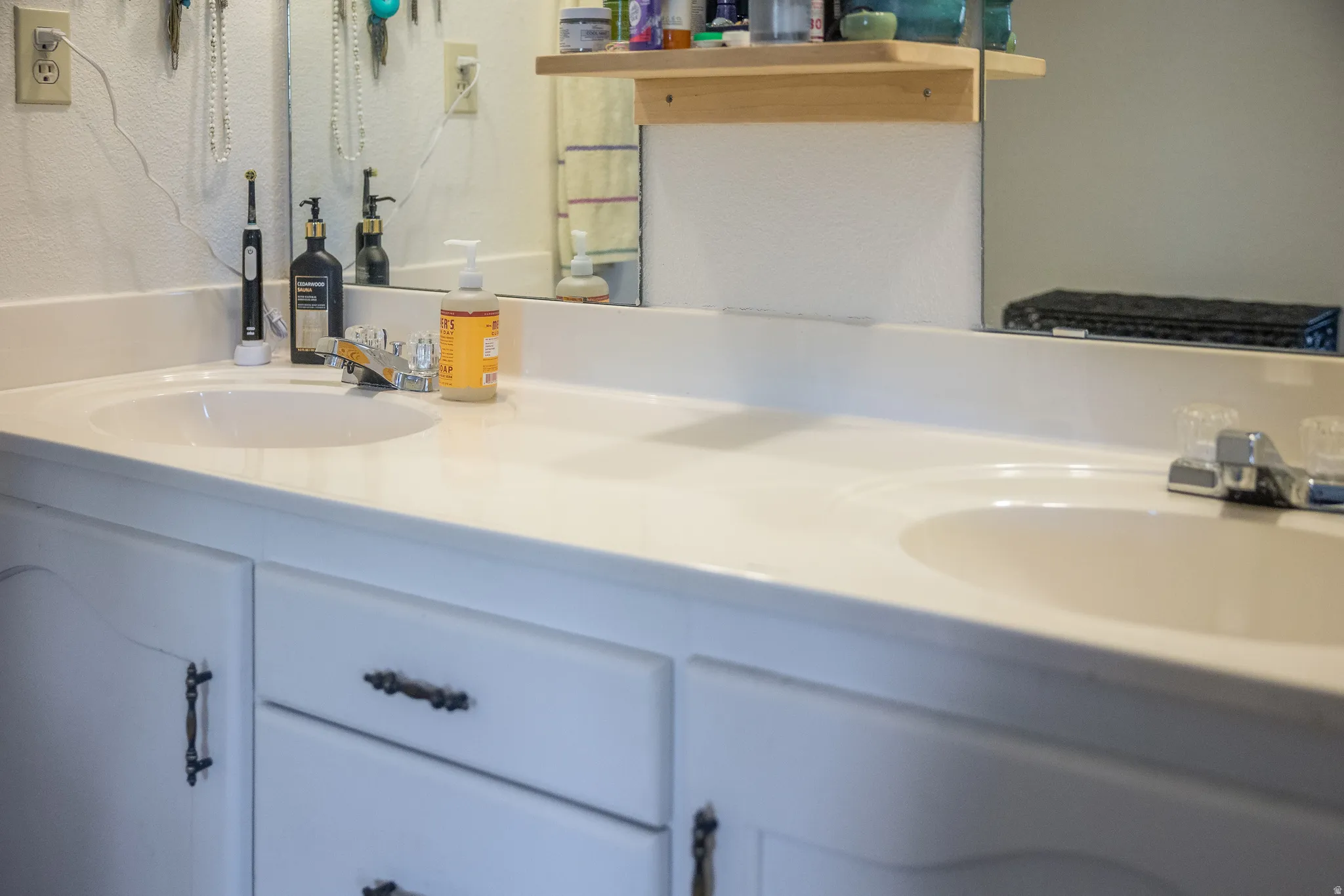 Double vanity with integrated sinks, white countertop, white cabinetry, dark bronze cabinet hardware, and a large mirror