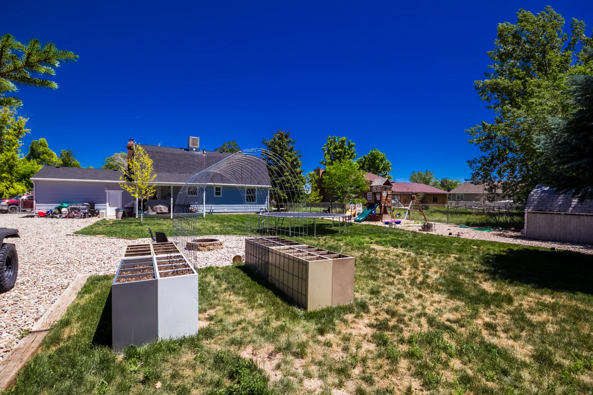 Expansive backyard featuring a gravel area, mature trees, a fire pit, and raised garden beds