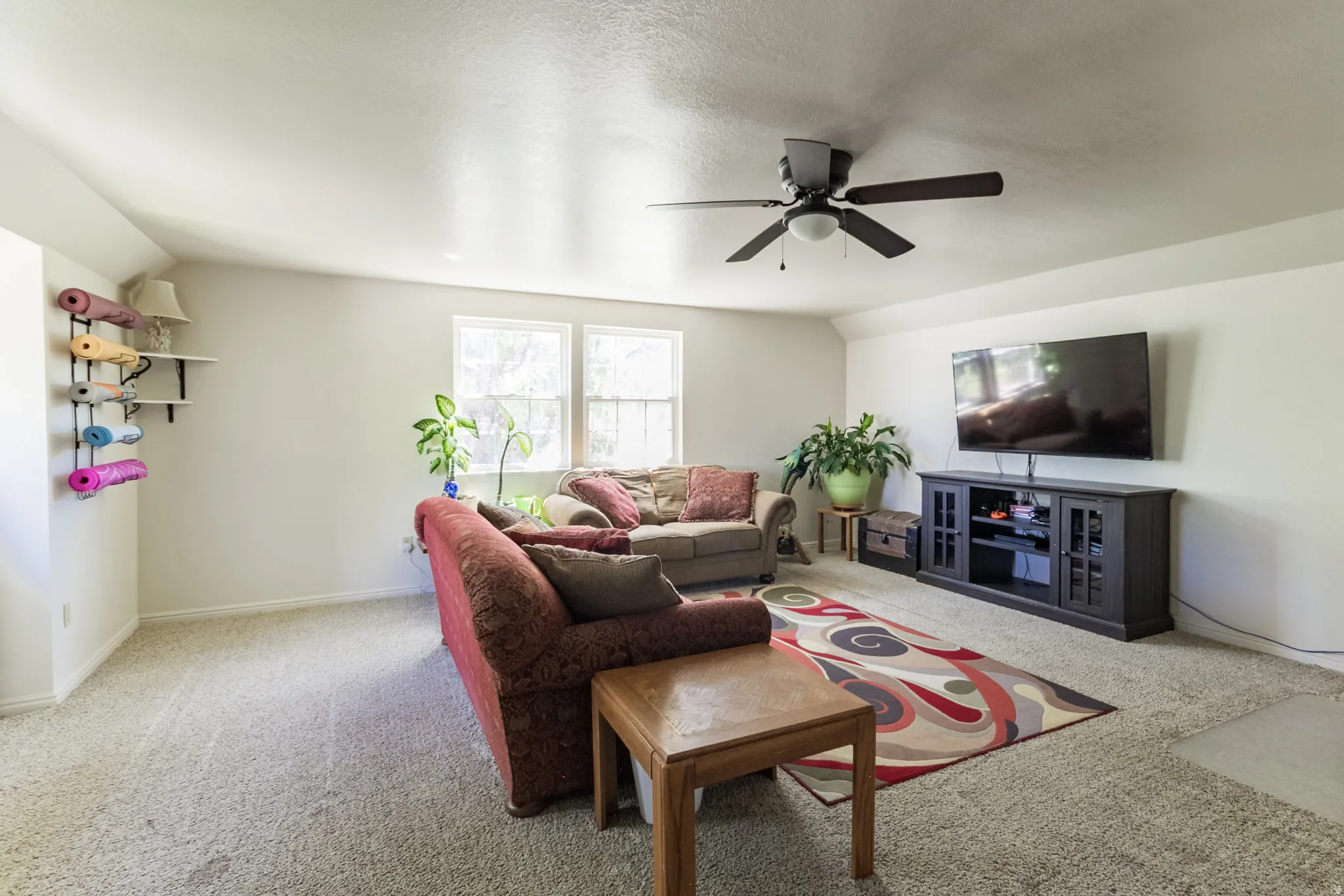 Spacious room featuring light-colored carpeting, multiple windows providing natural illumination, and a ceiling fan with integrated lighting