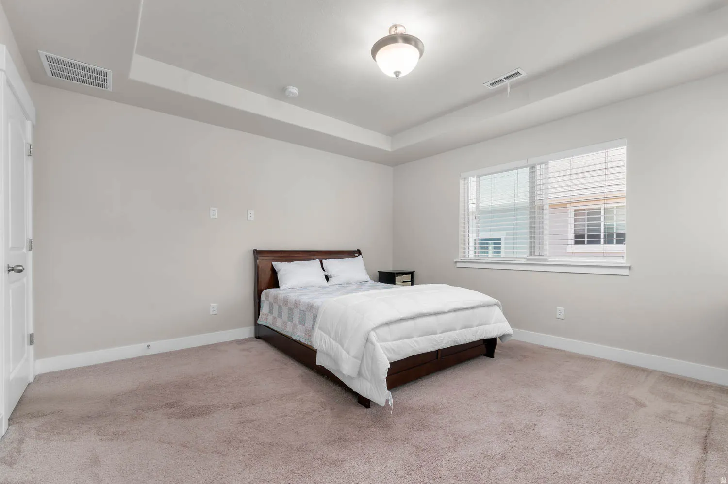 Spacious room featuring neutral carpeting, a tray ceiling, and a large window with blinds
