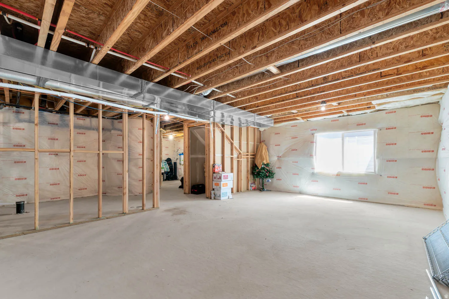 Unfinished basement featuring exposed wood joists and subflooring, framed interior walls, and a large window