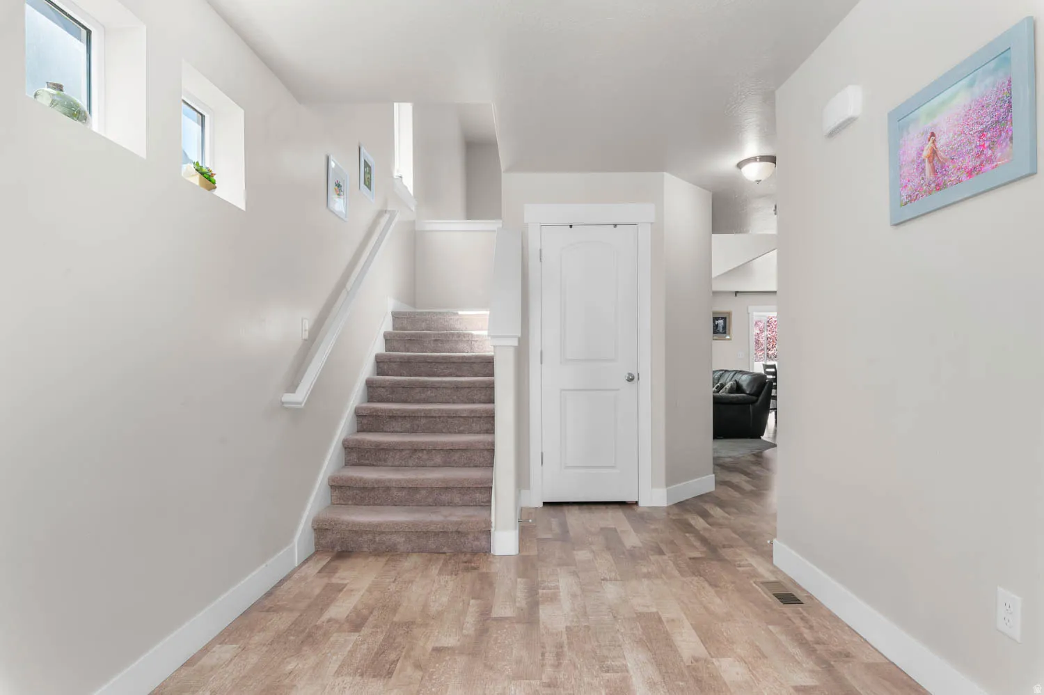 Entryway featuring wood-finish flooring, a carpeted staircase with white railing, a white panel door, and white trim throughout
