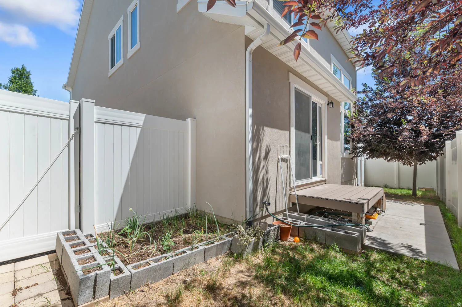 Rear exterior featuring a sliding glass door, elevated wood-finish deck, and concrete patio
