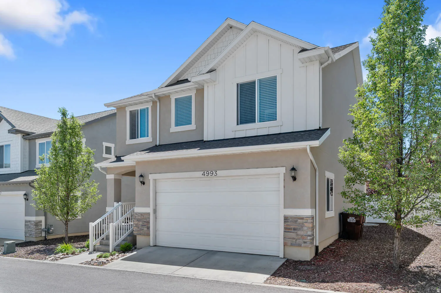 Contemporary multi-level exterior featuring light stucco siding, white board and batten accents, a single garage, stone veneer detailing, and exterior lighting fixtures