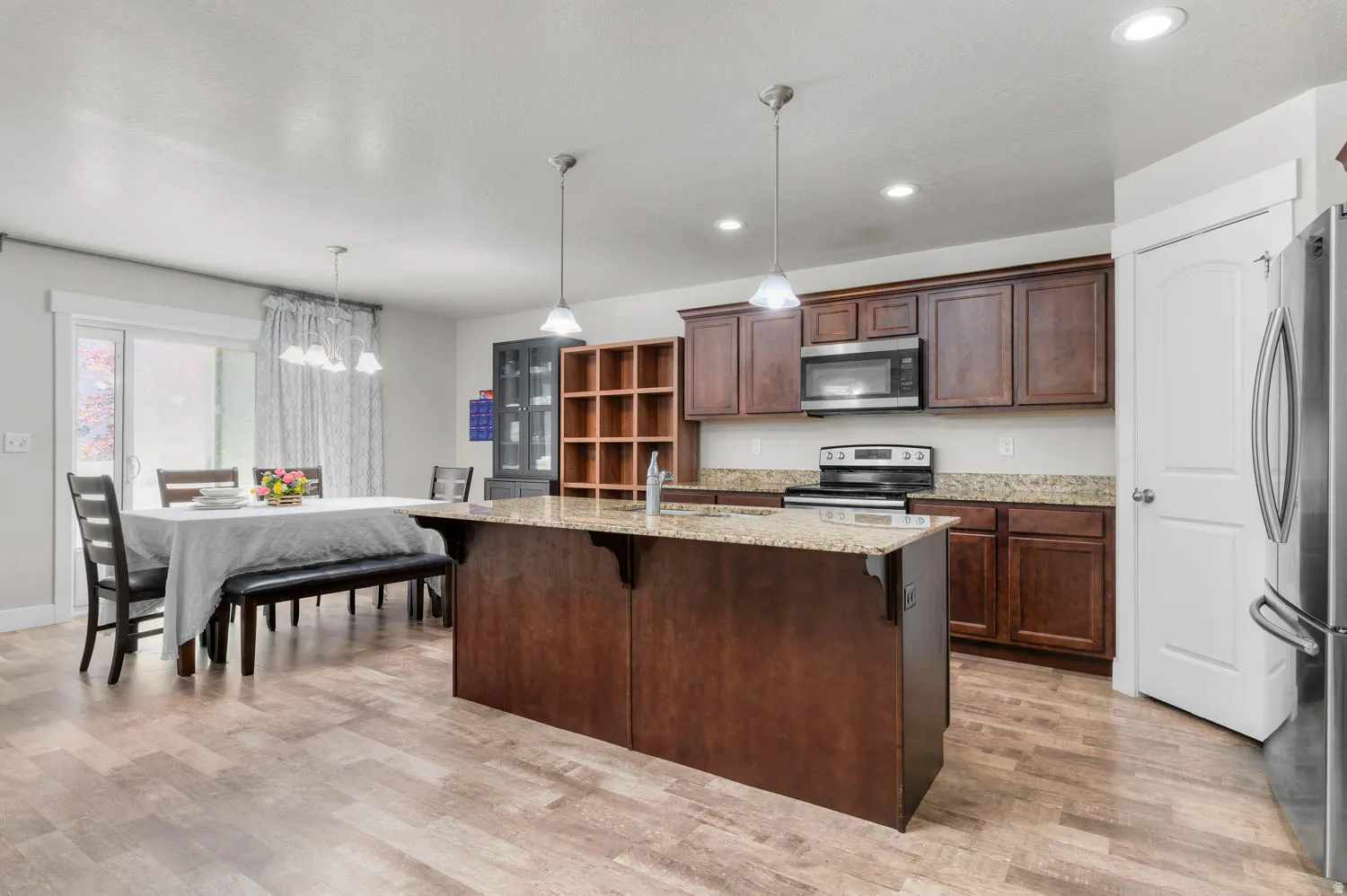 Expansive kitchen with a large island featuring pendant lighting, rich wood cabinetry, stainless steel appliances, and durable wood-finish flooring