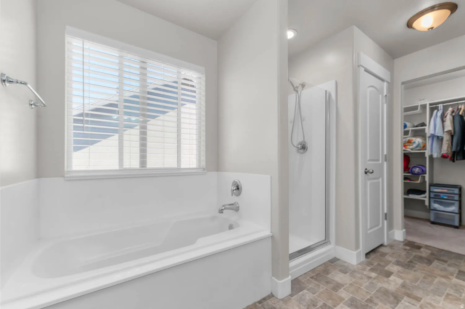 Soaking tub with chrome fixtures, window with blinds, stand-up shower with glass enclosure, and tile flooring