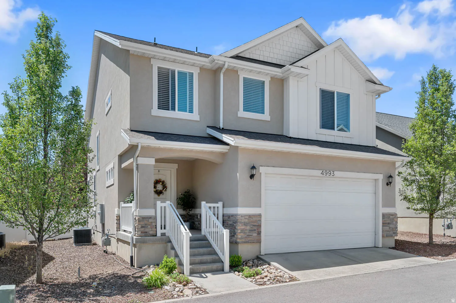 Two-story residence featuring a neutral stucco exterior with white trim accents and stone detailing