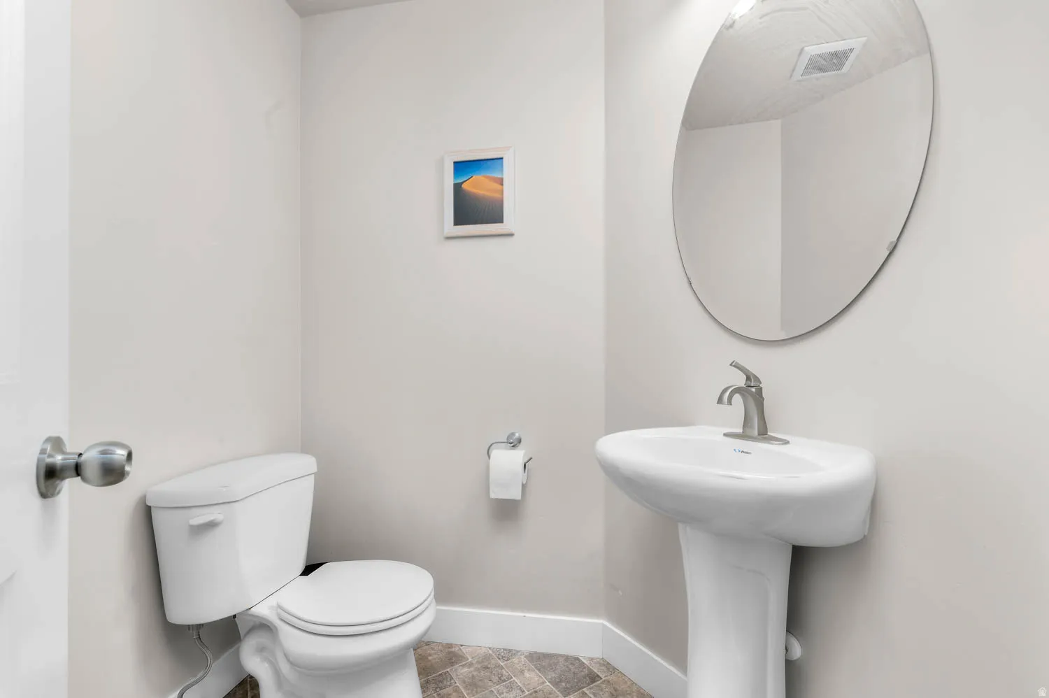 Pedestal sink with a brushed nickel faucet, an oval wall-mounted mirror, and a white toilet