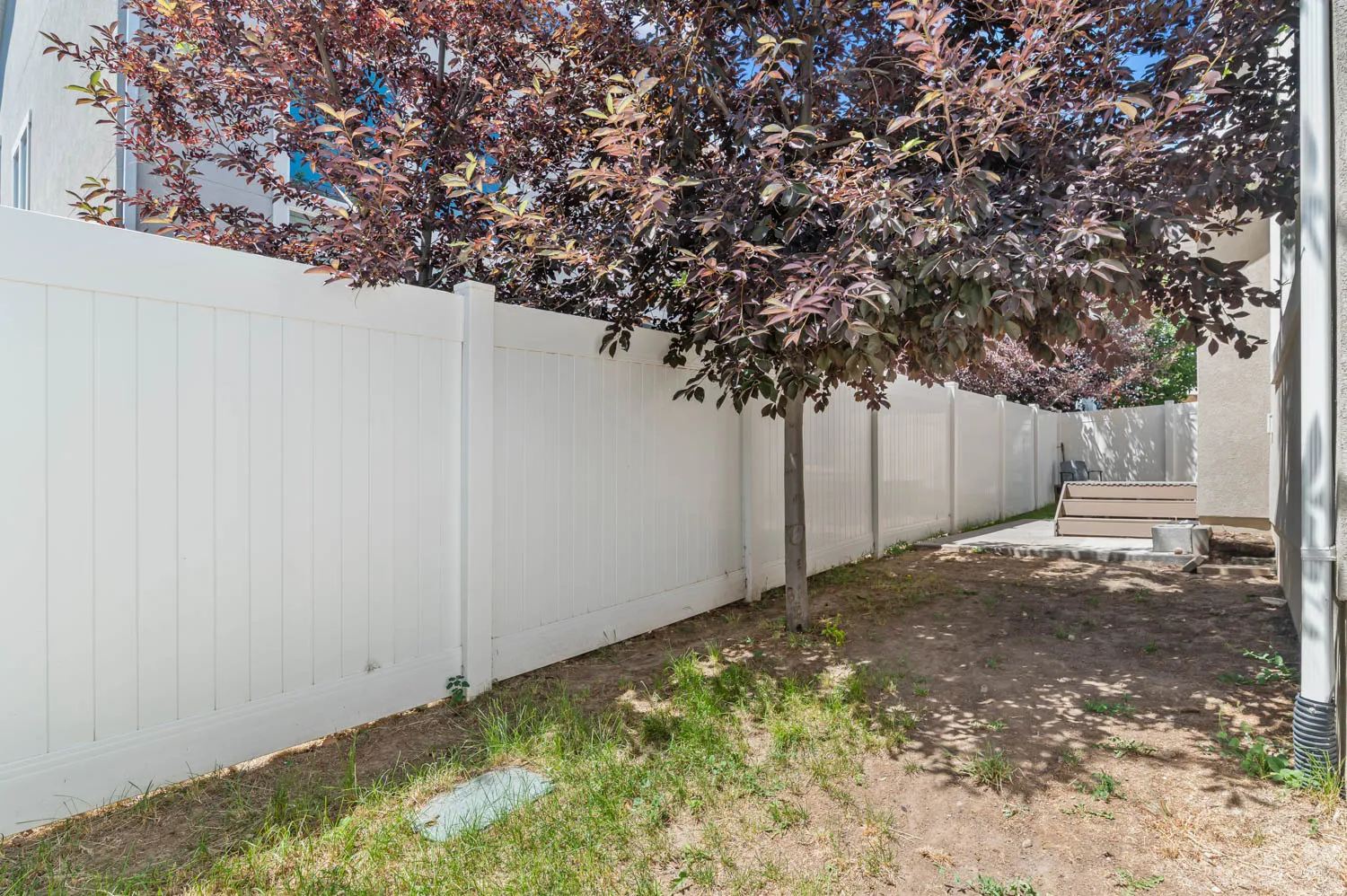 Private backyard featuring a white privacy fence, mature shade tree, and a concrete patio with wood-finish steps