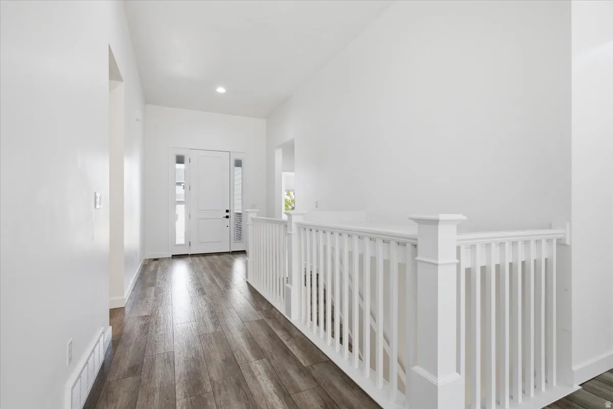 Bright entryway featuring wood-finish flooring, a white paneled front door with sidelights, a recessed ceiling light, and a white baluster railing