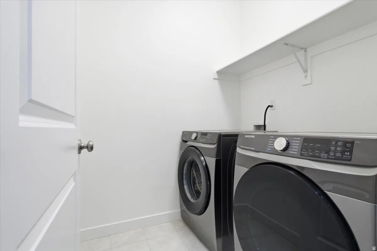 Dedicated laundry area featuring a front-loading washer and dryer, an overhead storage shelf, and light-toned flooring