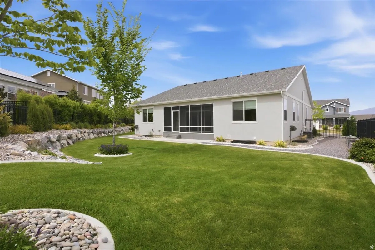 Expansive rear yard featuring a manicured lawn, established landscaping, and a screened porch