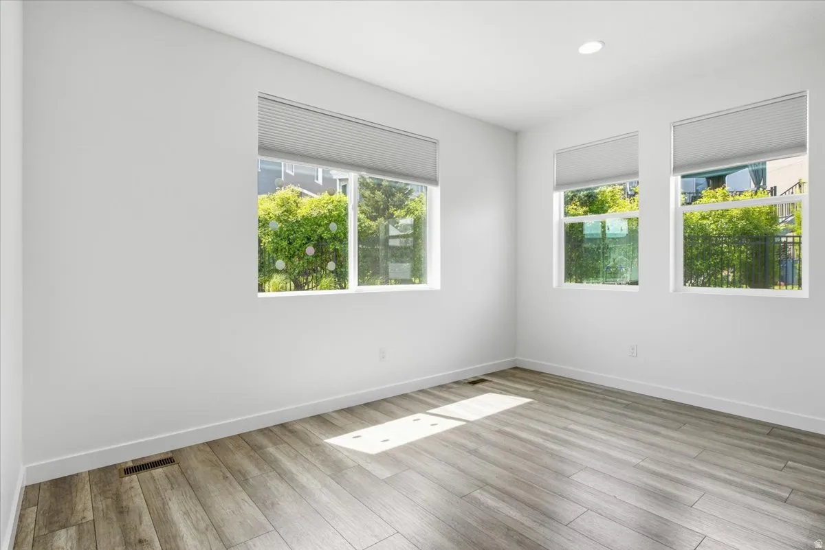 Room featuring wood-finish flooring, three windows with blinds, white walls, and recessed lighting