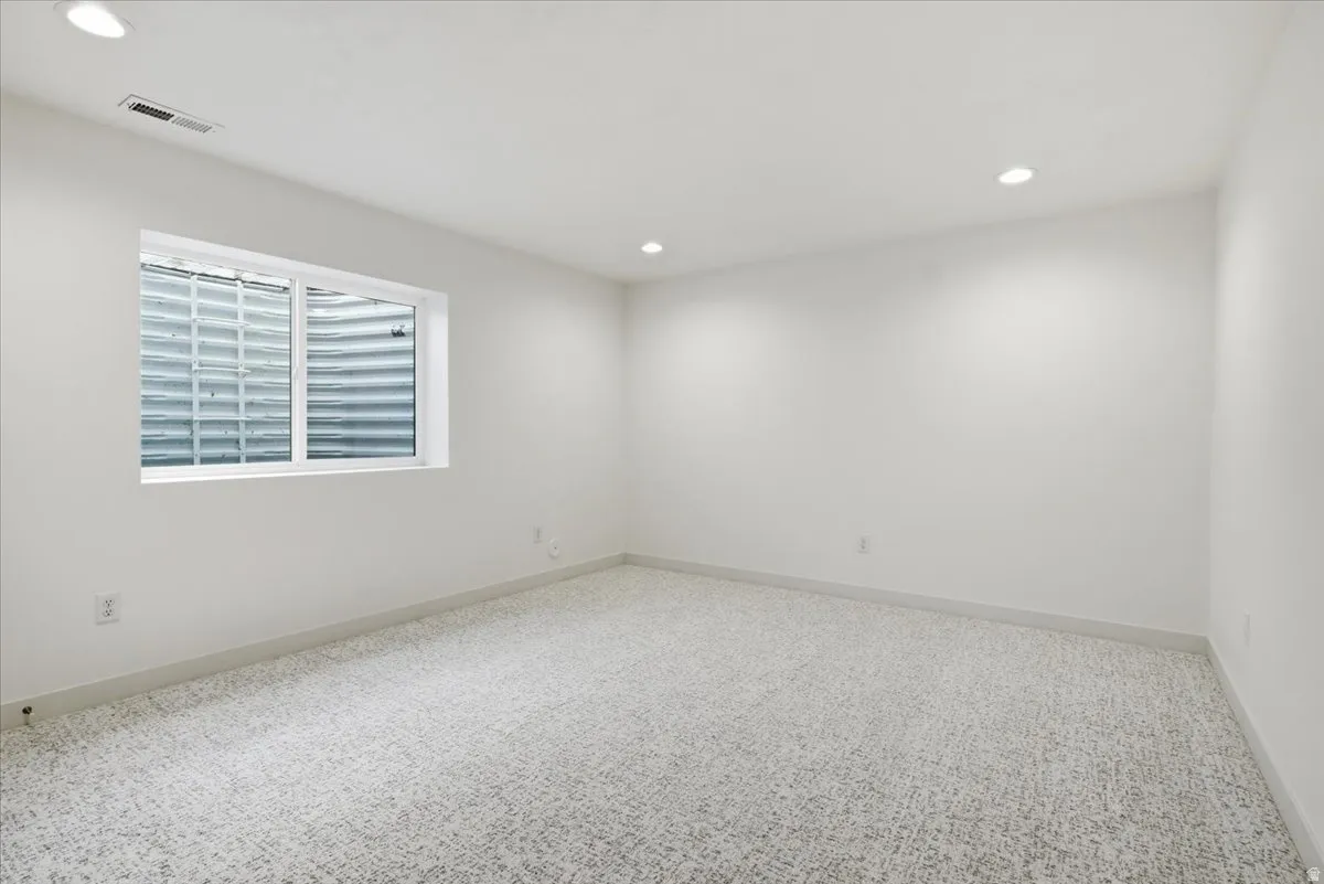 Bright room featuring a window with a white frame, light-colored patterned carpet, recessed ceiling lighting, and white walls