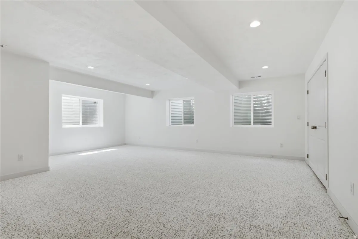 Spacious room with light-colored carpet, multiple egress windows, recessed lighting, and white trim